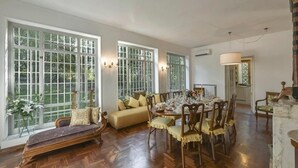 Ein Esszimmer mit einem großen Holztisch, gedeckt für sechs Personen, das von zwei Fenstern mit weißen Rahmen begrenzt wird.