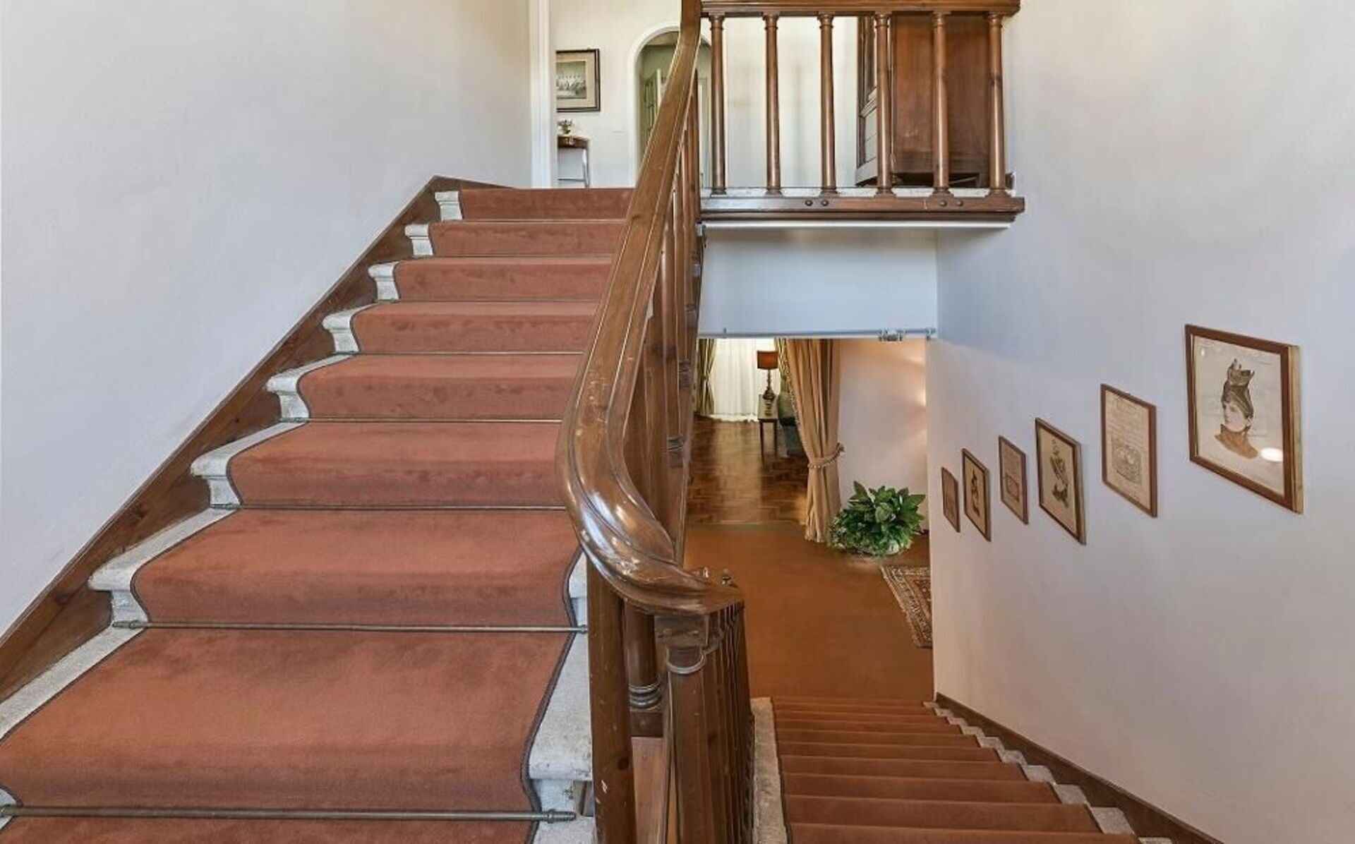 A grand staircase with a wooden handrail and a landing with framed pictures.