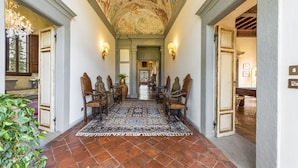 Un couloir avec un tapis à motifs, des chaises en bois et une peinture murale au plafond.