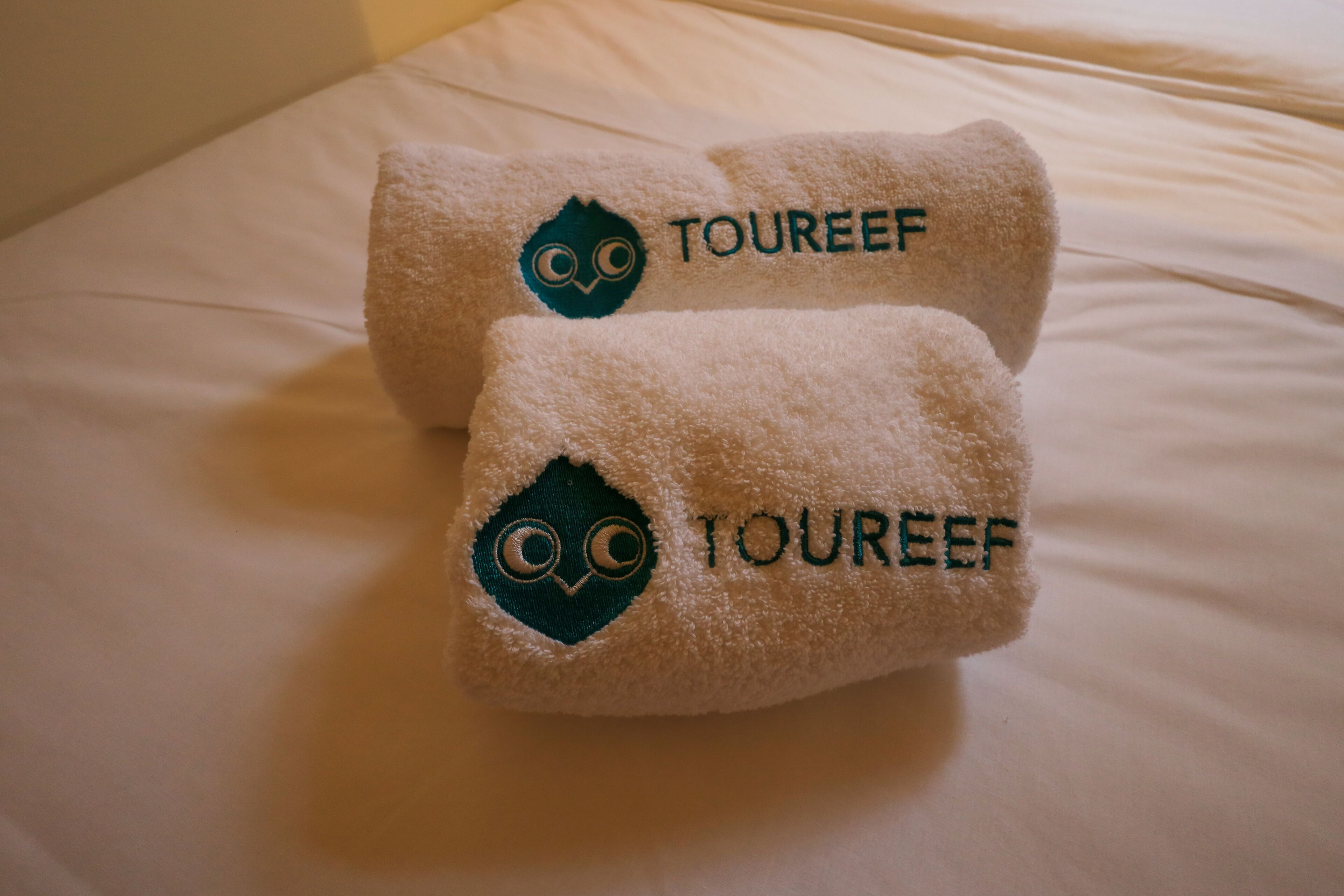 Two towels with embroidered owl logos and the word "TOUREEF" on a bed.