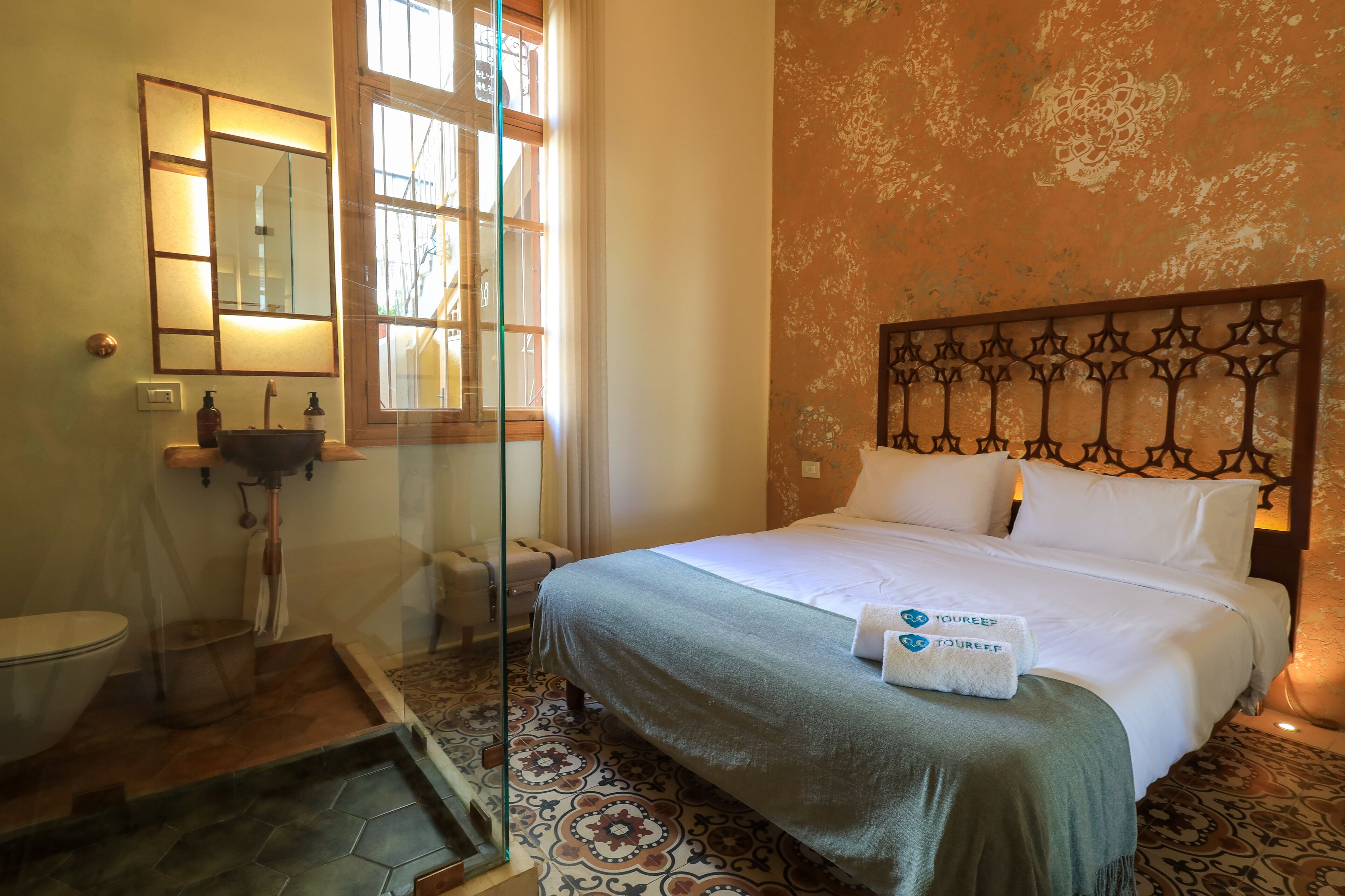 A hotel room with a bed, a bathroom with a sink and mirror, and a patterned floor.