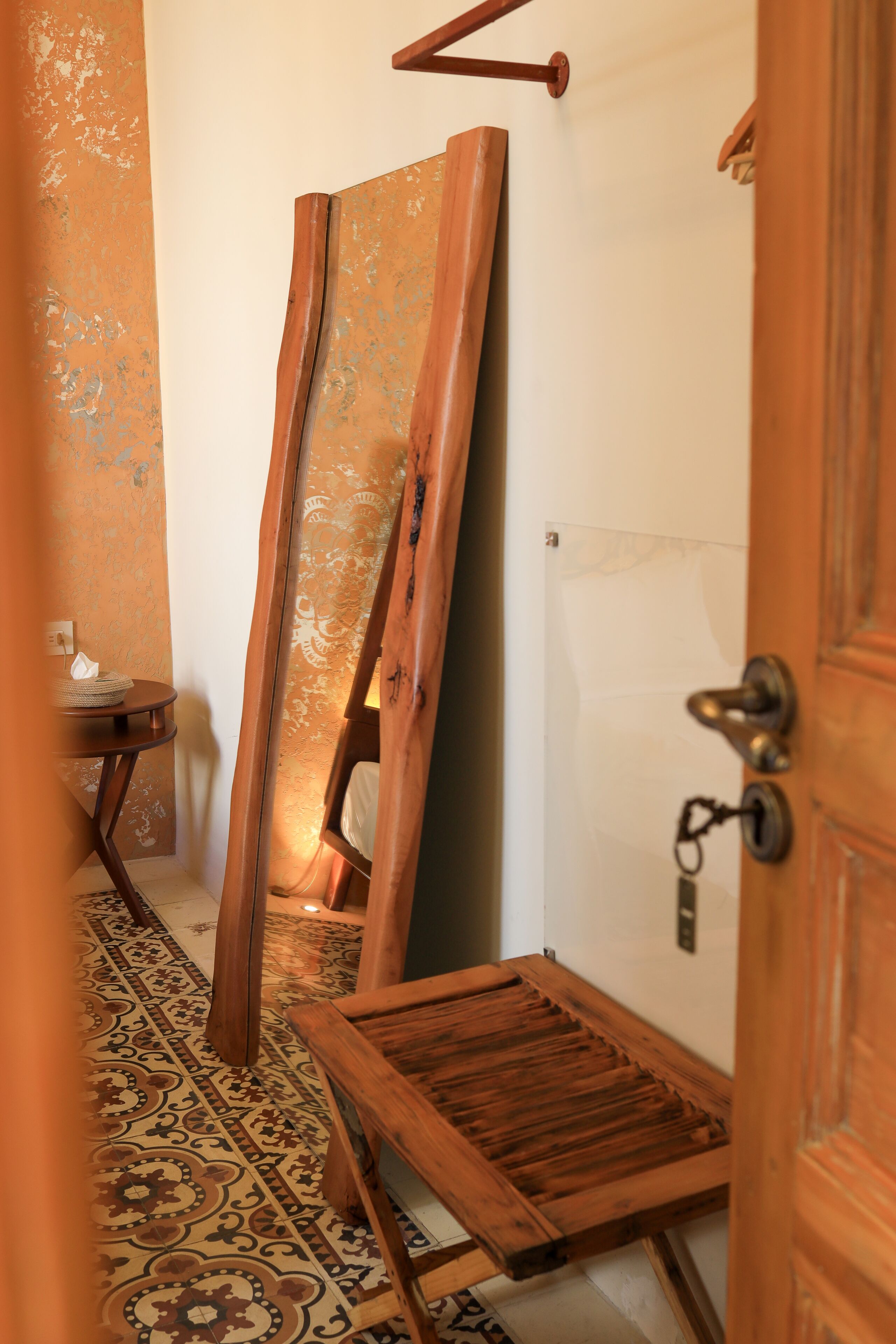 Ein schmaler Flur mit einer Holzbank, einem an der Wand lehnten großen Spiegel und einem kleinen Tisch mit einer Lampe.