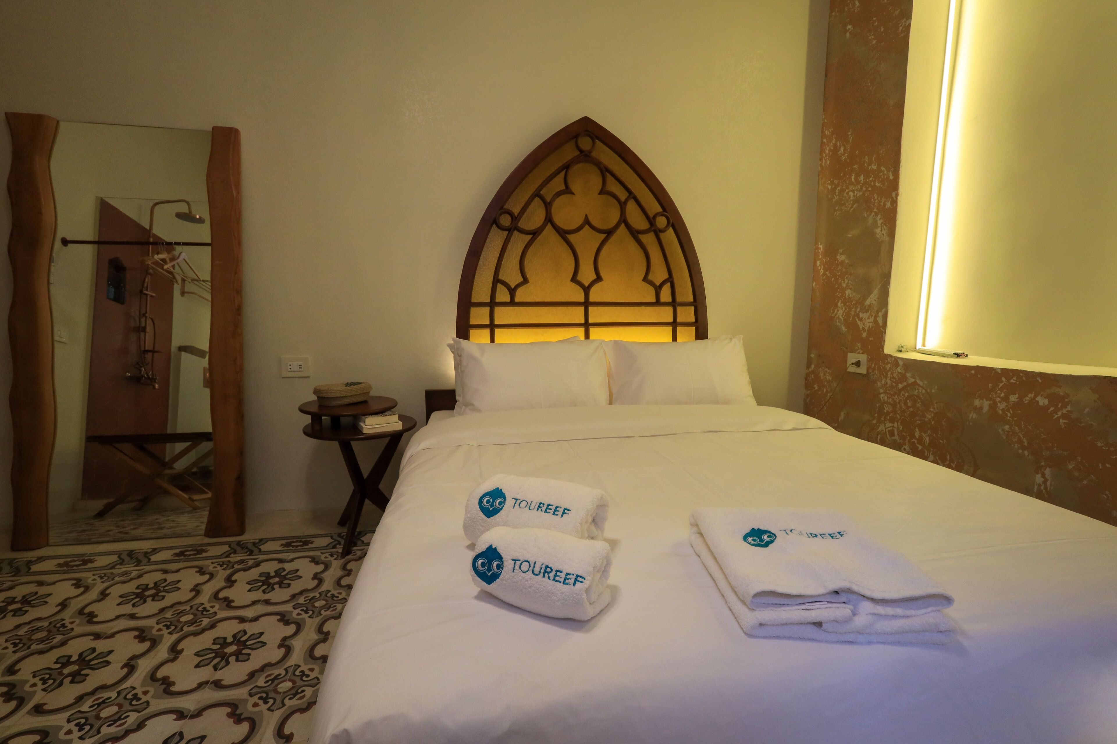 Una habitación de hotel con una cama grande, un cabecero de madera y dos toallas con el logotipo "TOUREEF".