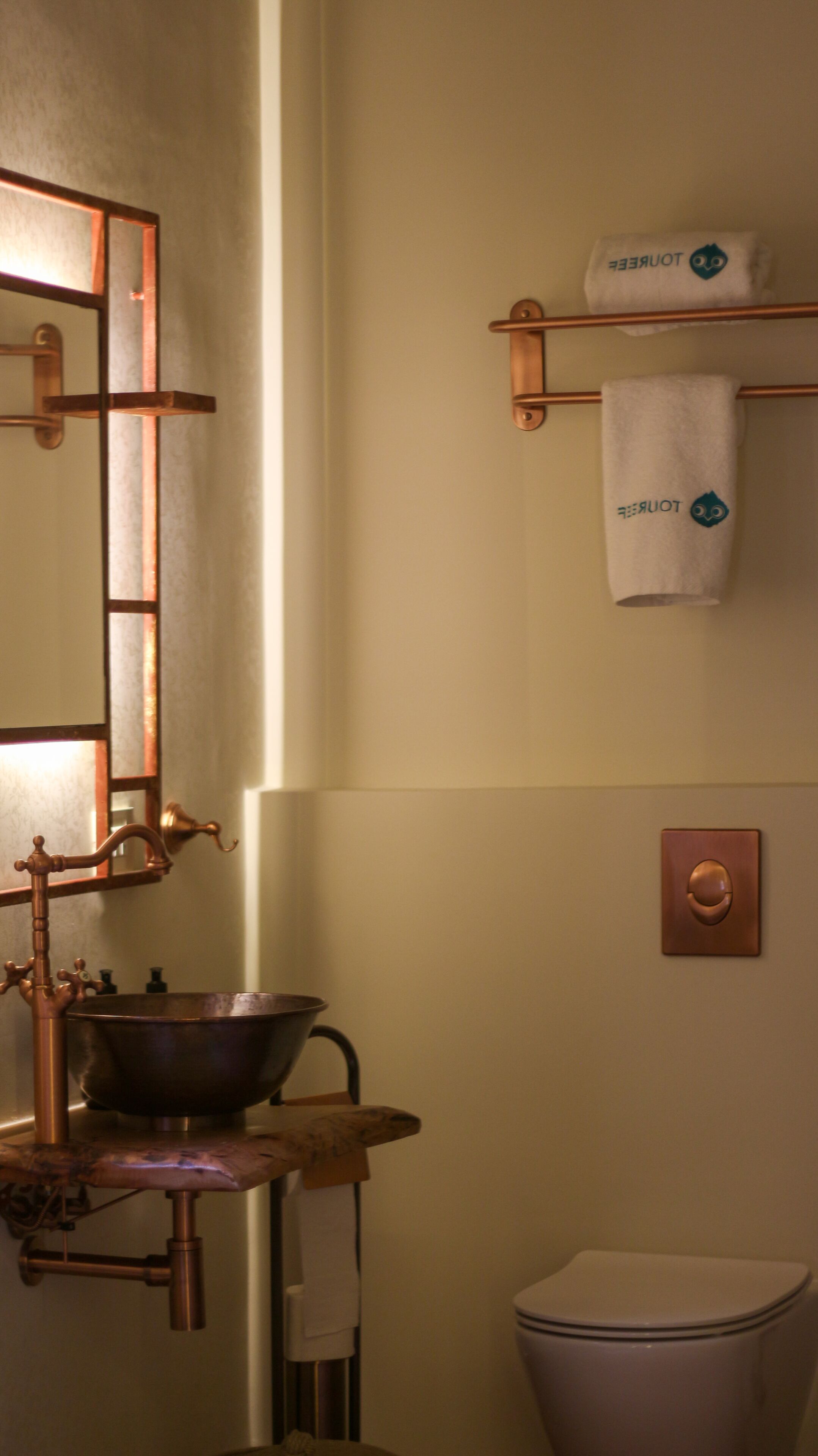 A bathroom with a copper faucet, a basin, a towel rack with a towel, and a toilet.