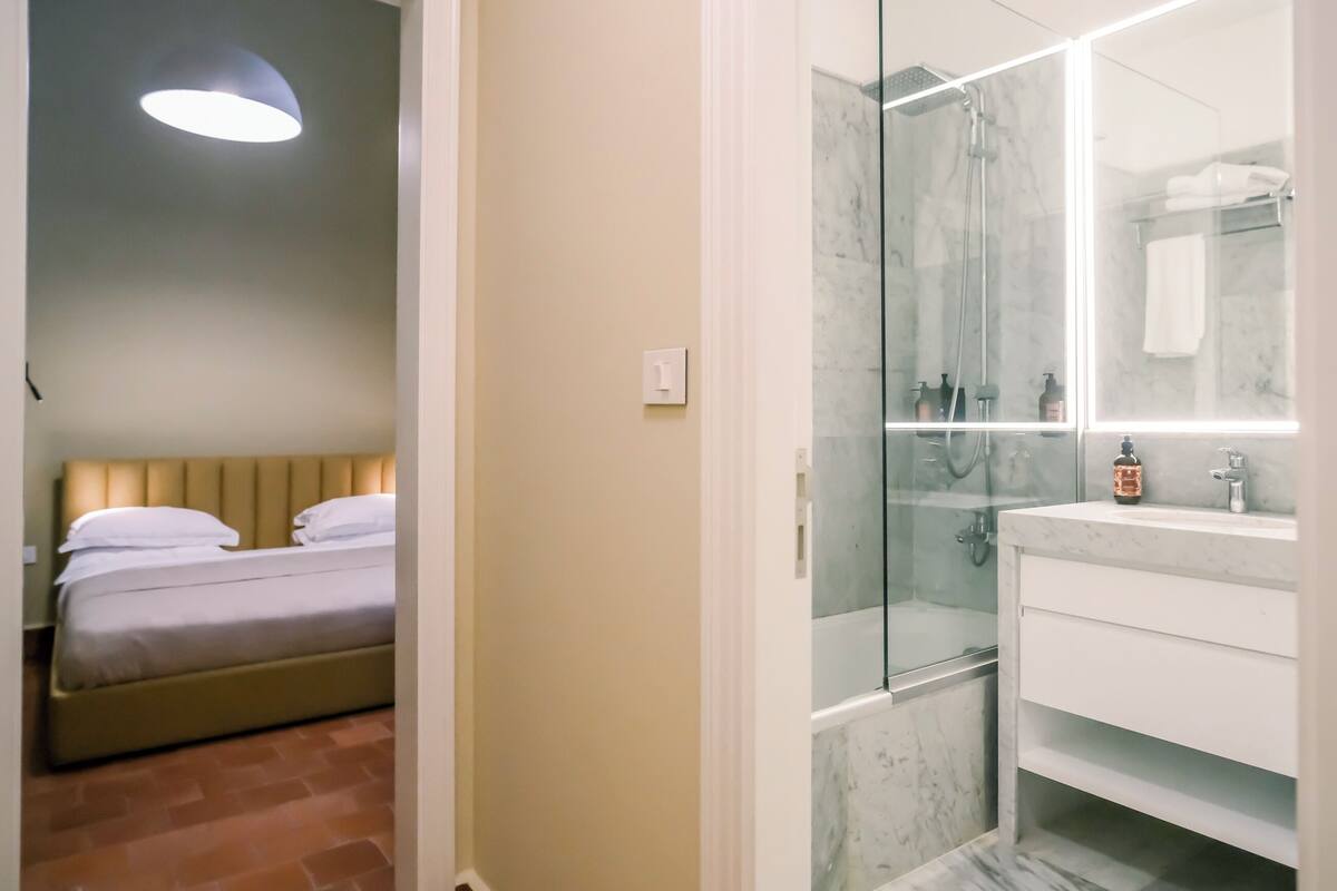 Un dormitorio con cama y un baño con ducha de vidrio y lavamanos de mármol.