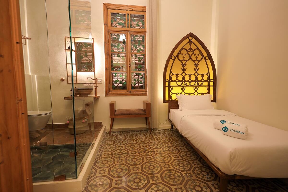 Un dormitorio con cama, una silla, un ventanal con marco decorativo y zona de ducha.