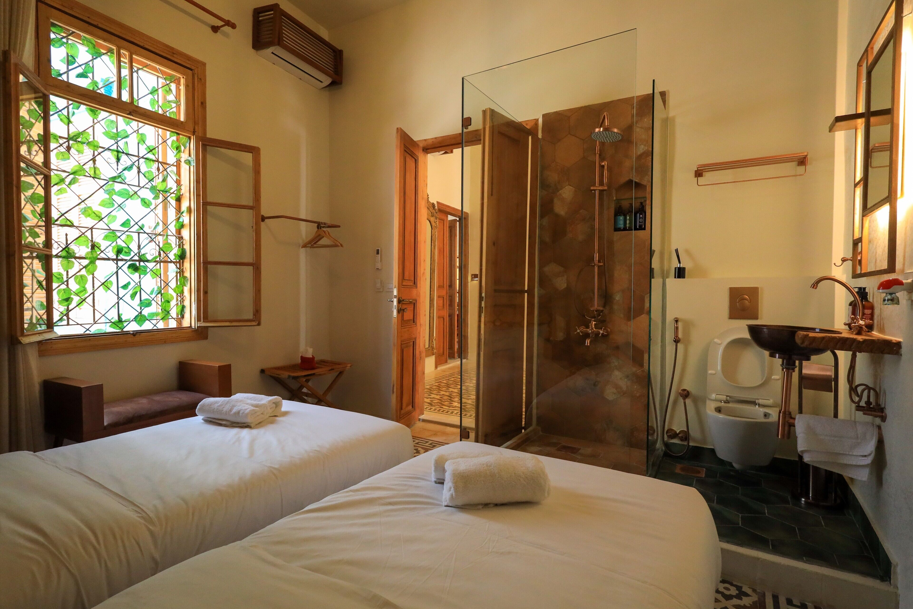 Ein Hotelzimmer mit zwei Betten, einer Dusche, einem Waschbecken und einem Fenster mit Blick auf Grünflächen.