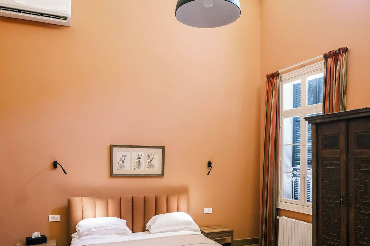 Un dormitorio con una cama, una mesita de noche, aire acondicionado instalado en la pared, una ventana con cortinas y un suelo con diseño.