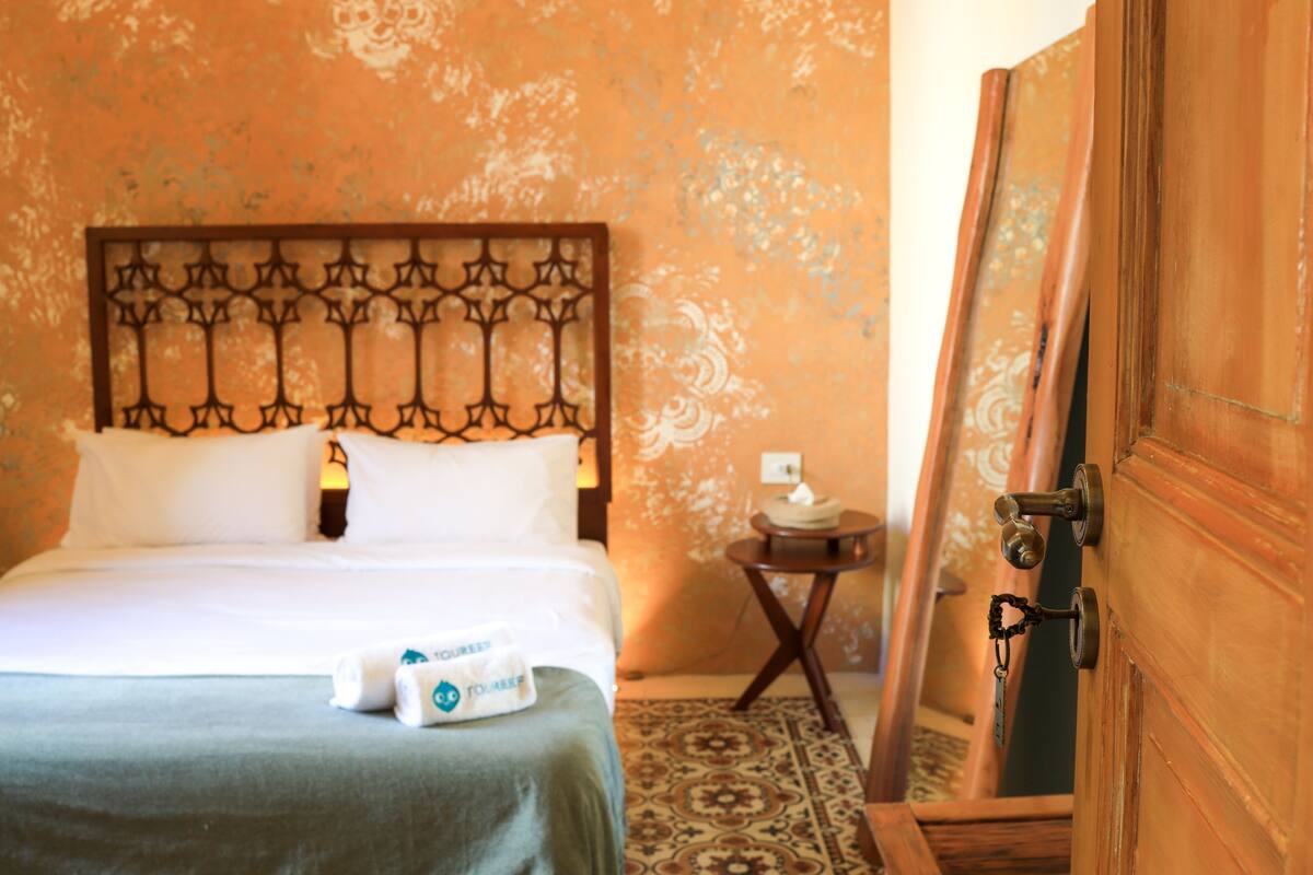 Una habitación de hotel con una cama, una mesita de noche con lámpara y una puerta de madera.