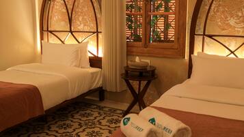 A hotel room with two beds, a small round table with a tissue box, and a window with a view of greenery.