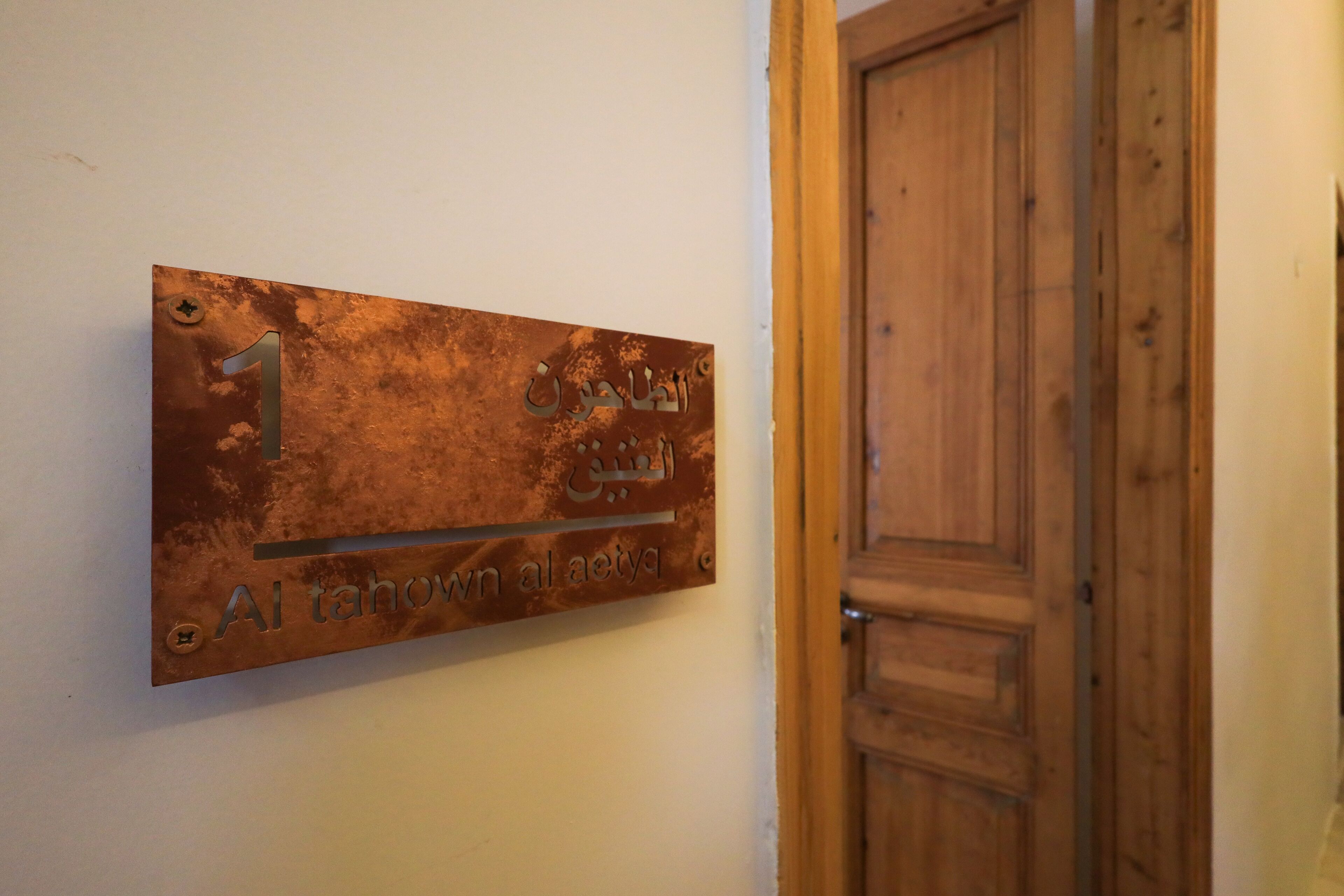 Un letrero de metal con texto en árabe y el número '1' en una pared, junto a una puerta de madera.
