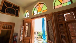 A room with wooden doors and windows, a fire extinguisher, and a view of a balcony with a blue railing. - Beit Toureef - HOME (Beirut)