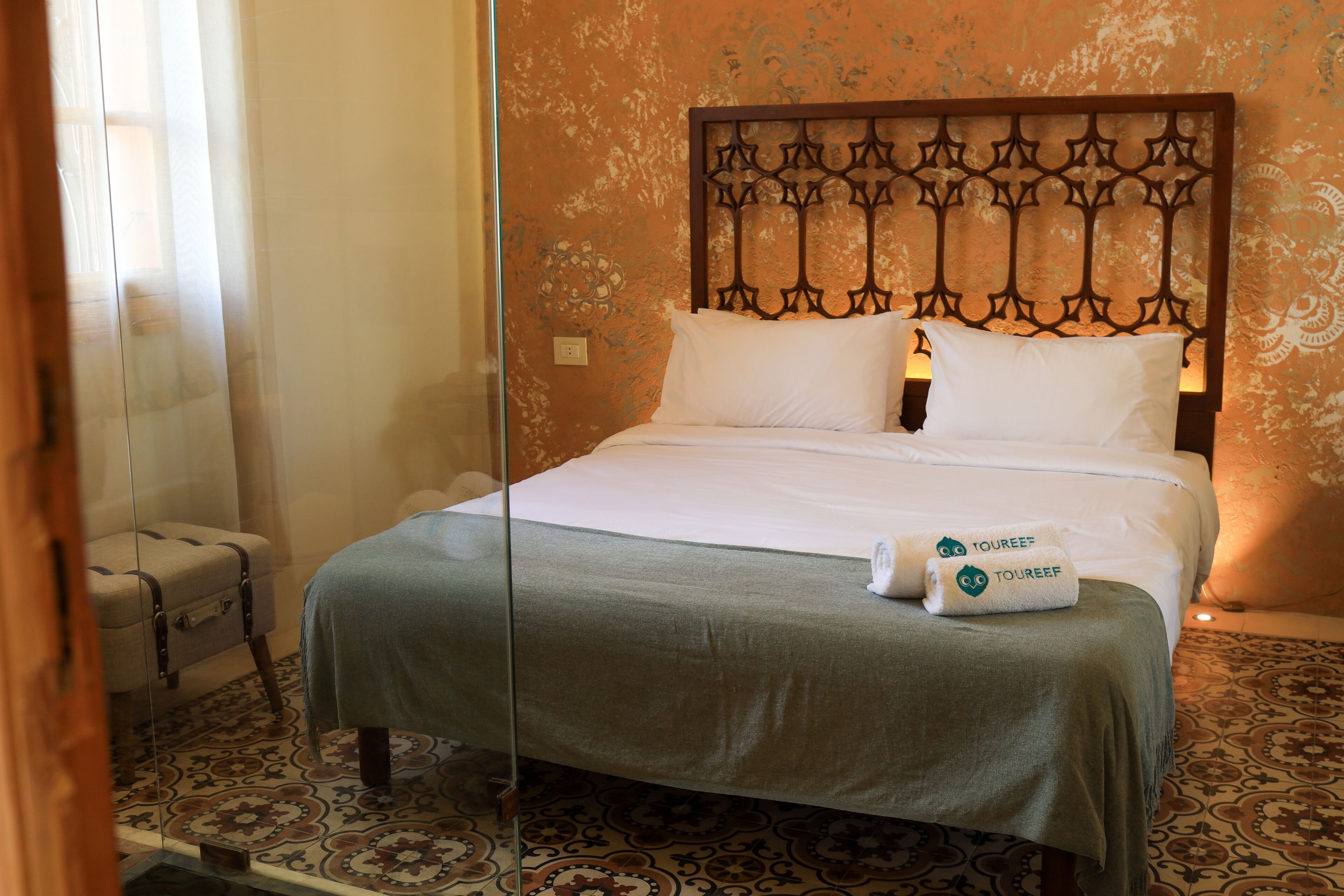 A hotel room with a bed, a suitcase, and a patterned floor.