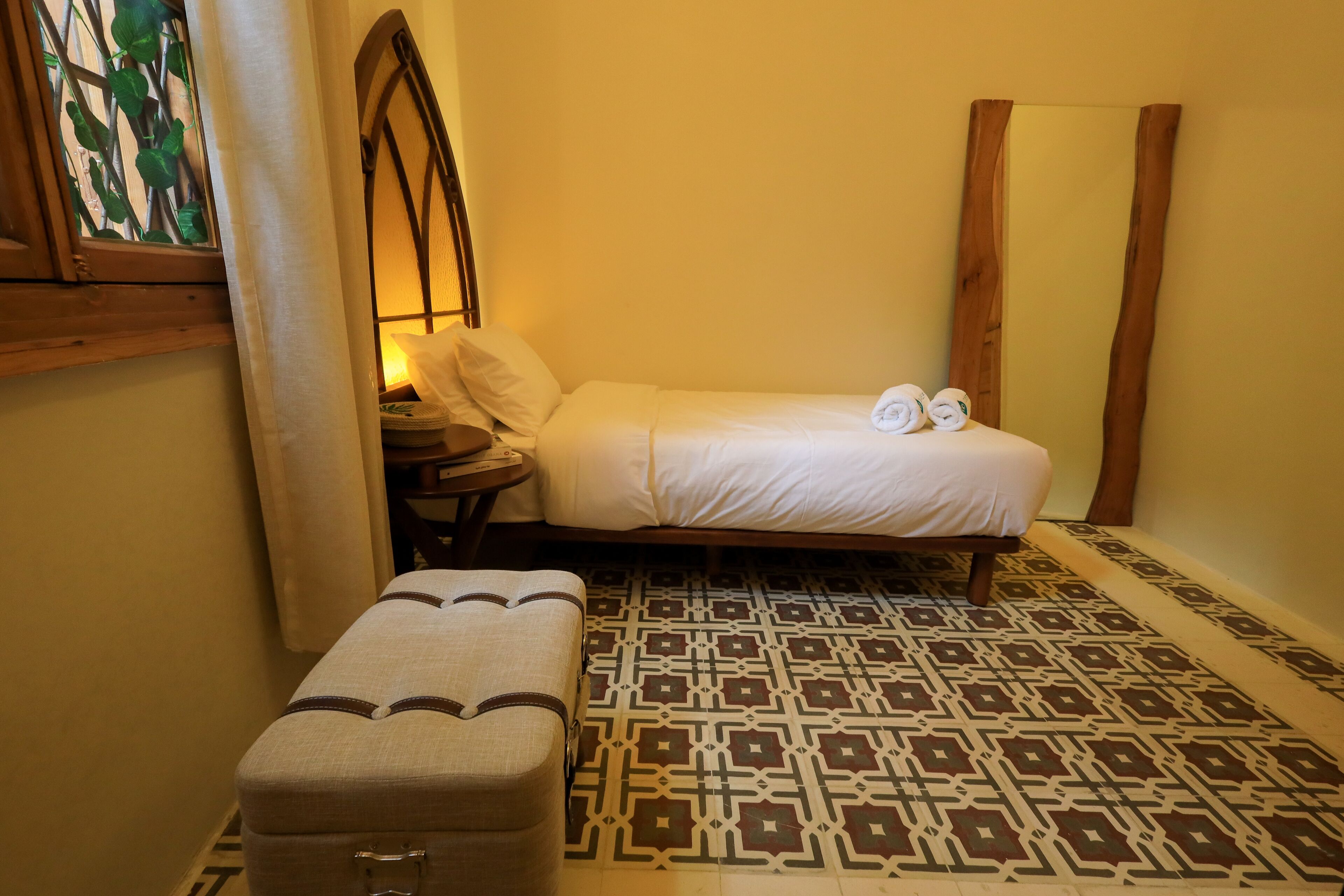 Una habitación pequeña y acogedora con una cama, un banco y un suelo estampado.