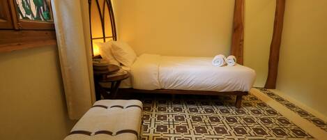 A small, cozy room with a bed, a bench, and a patterned floor.