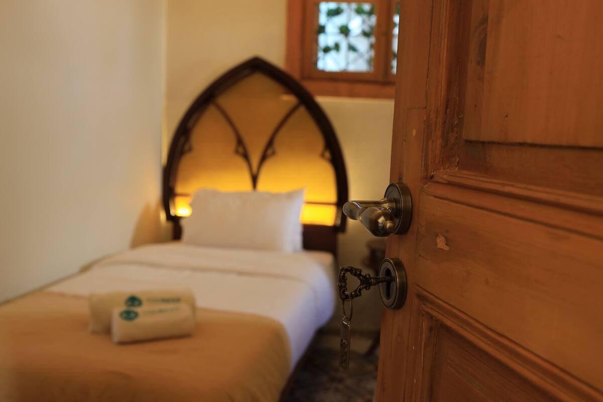 Un dormitorio con una puerta de madera, una cama con cabecera blanca y una mesita de noche con lámpara.