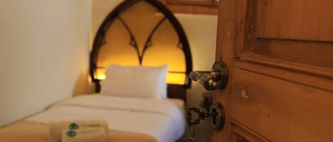 Un dormitorio con una puerta de madera, una cama con cabecera blanca y una mesita de noche con lámpara.