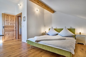 Een slaapkamer met een houten vloer, een groen bed, twee nachtkastjes met lampen, en een houten deur.