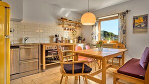 Une cuisine compacte dotée d’un four encastré, un coin repas avec une table et des chaises en bois, et une fenêtre donnant sur la campagne.