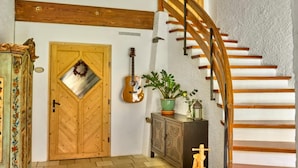 Un escalier avec des marches en bois et une rampe, une porte en bois ornée d’une fenêtre en forme de losange, et une guitare accrochée au mur.
