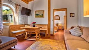 A cozy room with a wooden bench, a table with a vase of flowers, a sofa, a TV, and a painting on the wall. - "Hennenkobel" Apartment with Terrace (Am Kaisersteig Vacation Rentals) (Zwiesel)