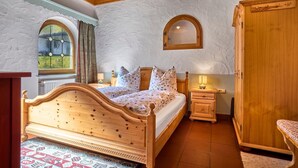 A bedroom with a wooden bed, a nightstand, a wardrobe, a mirror, and a window with curtains. - "Hennenkobel" Apartment with Terrace (Am Kaisersteig Vacation Rentals) (Zwiesel)