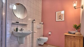 A bathroom with a sink, mirror, toilet, and a wooden cabinet with a vase. - "Hennenkobel" Apartment with Terrace (Am Kaisersteig Vacation Rentals) (Zwiesel)