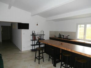 A modern kitchen with a wooden bar and stools, a built-in bookshelf, and a window with a view of the outside. - Gîte à Caromb (Caromb)
