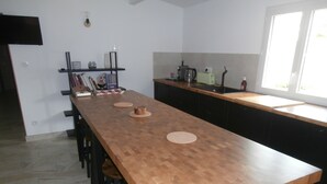 Een moderne keuken met een lange houten tafel, zwarte barkrukken en een inbouwoven.