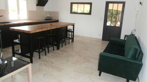 Een moderne keuken met een houten eiland en barstoelen, een groene bank, en een deur met uitzicht.