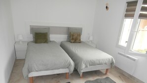 Een slaapkamer met twee bedden, een nachtkastje, een lamp, een radiator en een raam.