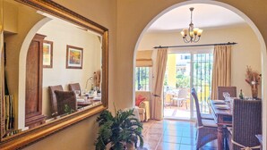 A dining area with a large mirror, wicker chairs, a chandelier, and a view through an arched doorway.