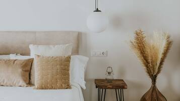 Een slaapkamer met een bed, kussens, een nachtkastje met een lamp en een vaas met pampa gras.