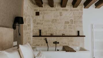 Ein Badezimmer mit Steinwand, Holzbalken, einer Badewanne und einem Regal mit Dekoration.