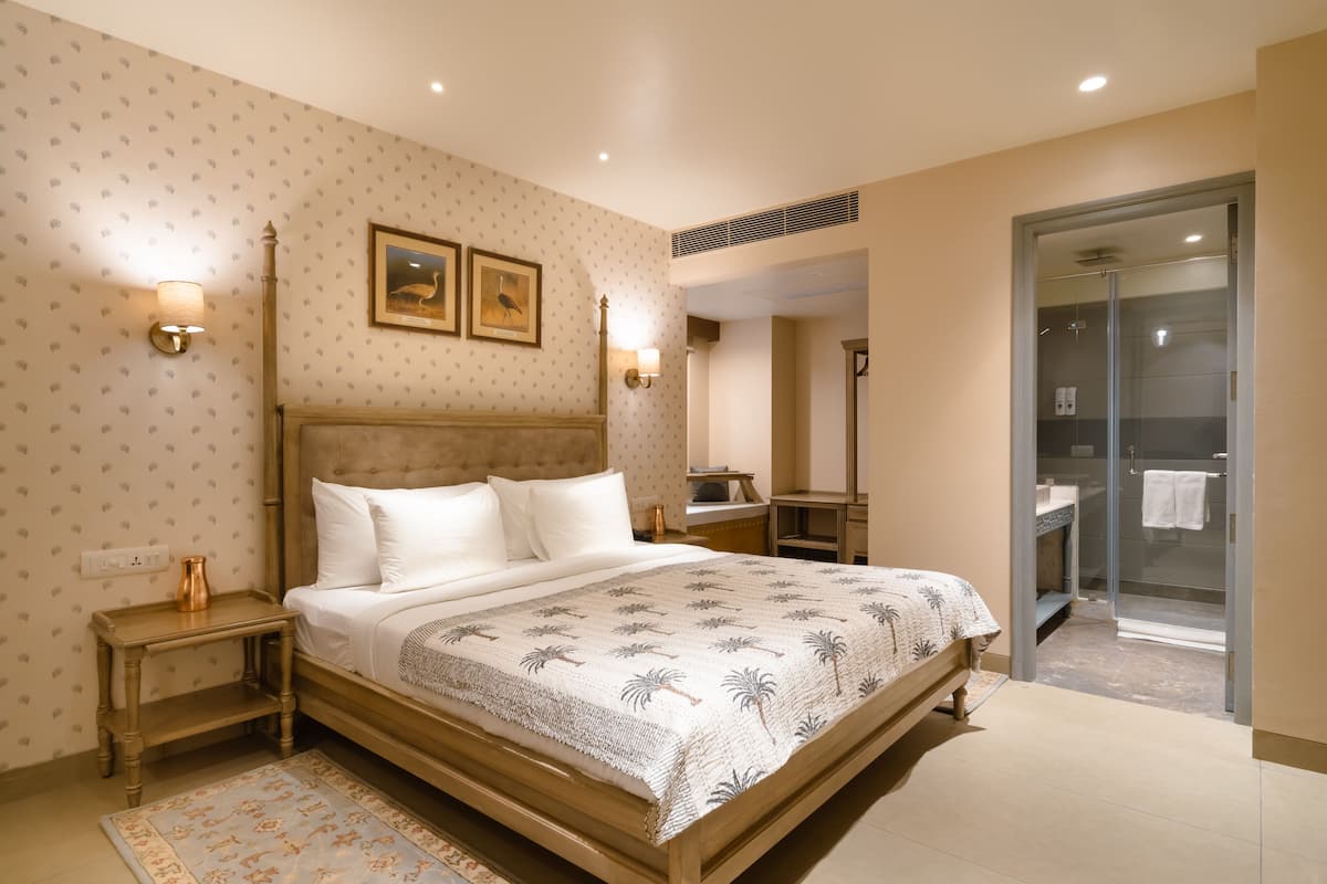 Un dormitorio con una cama grande, una mesita de noche, una lámpara de noche, un estante en la pared y una zona de ducha visible a través de una puerta de cristal.