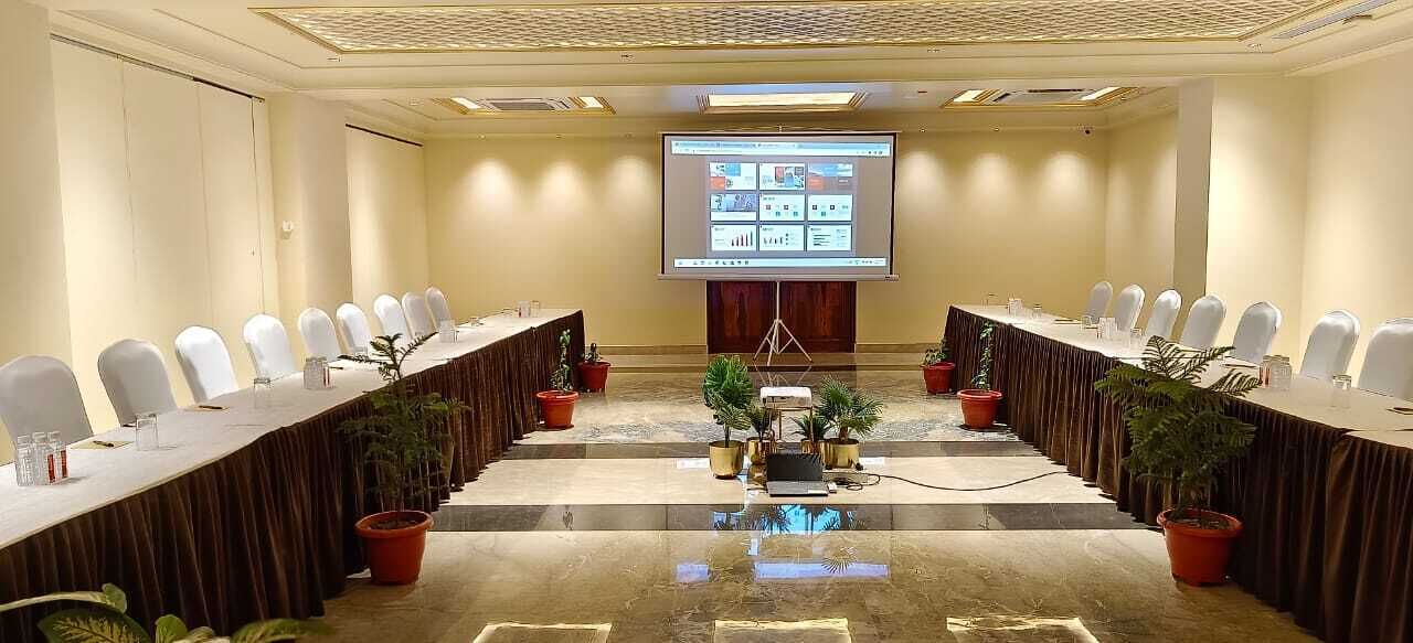Une salle de conférence avec une longue table, des chaises blanches et un écran de projection diffusant une présentation.