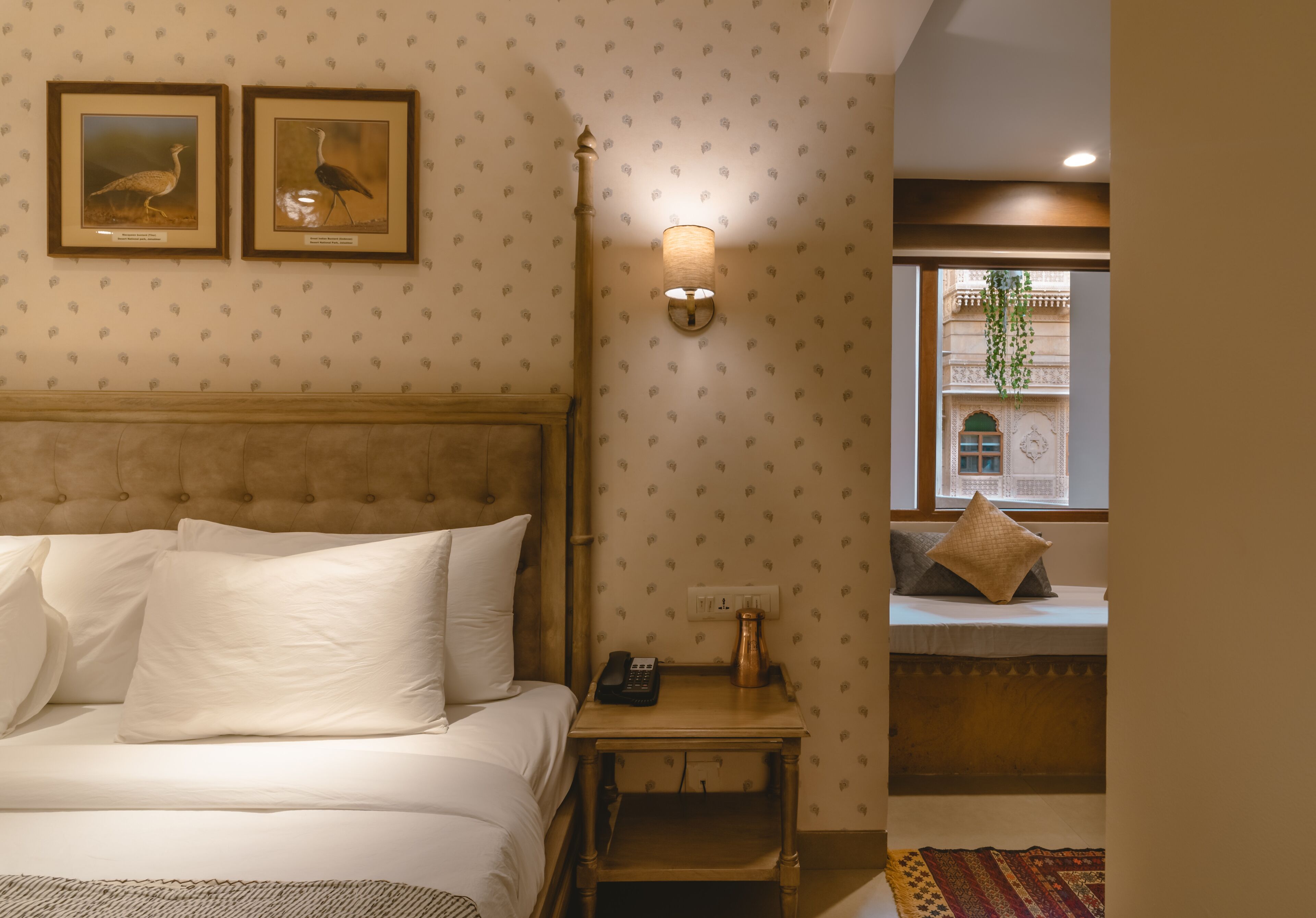 Una habitación de hotel con una cama, una mesita de noche con lámpara y dos cuadros en la pared.