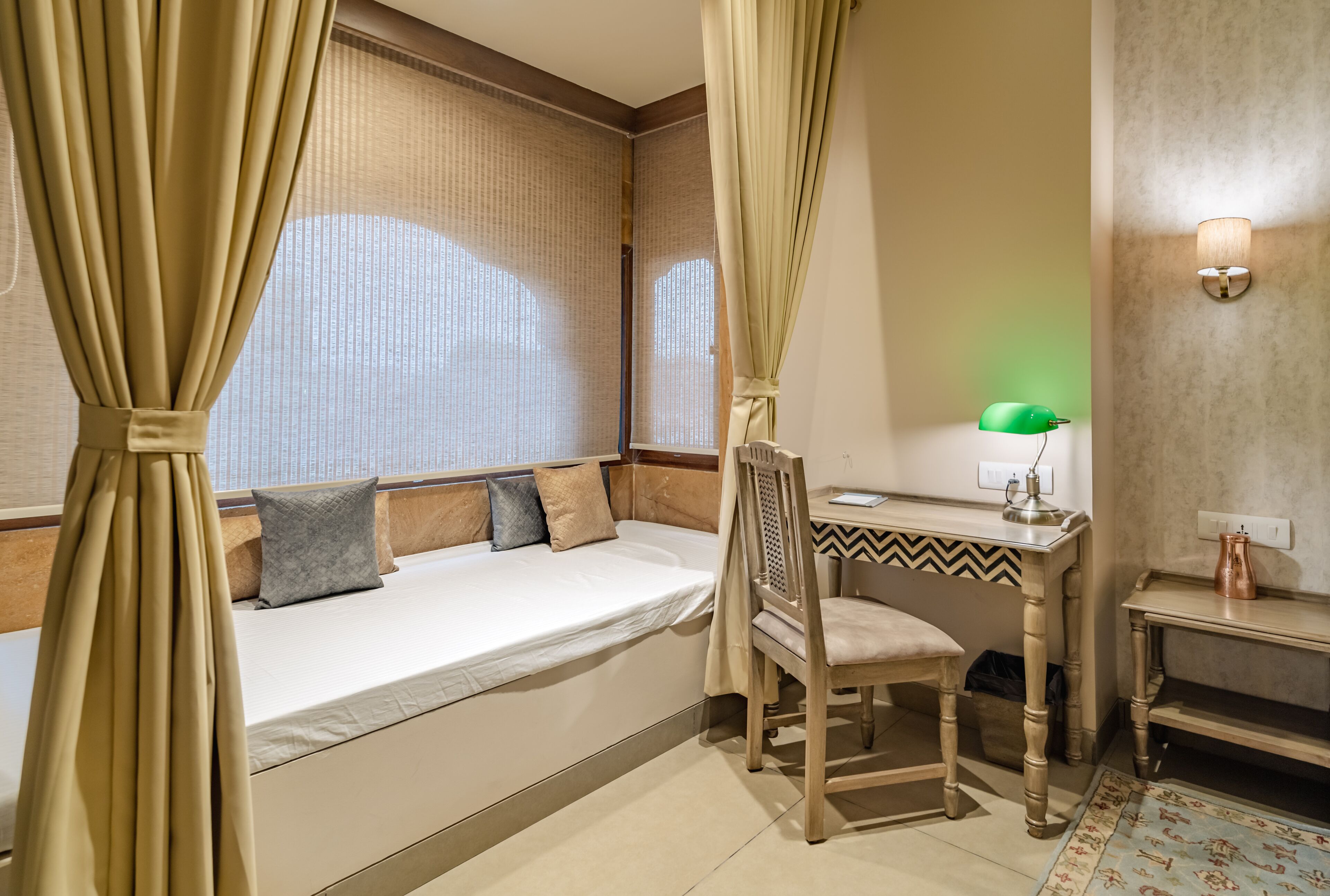 A bedroom with a bed, a desk, a chair, a lamp, and a wall-mounted light fixture.