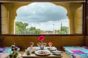 A table with various dishes and a vase of flowers, set against a window with a view of trees and buildings.
