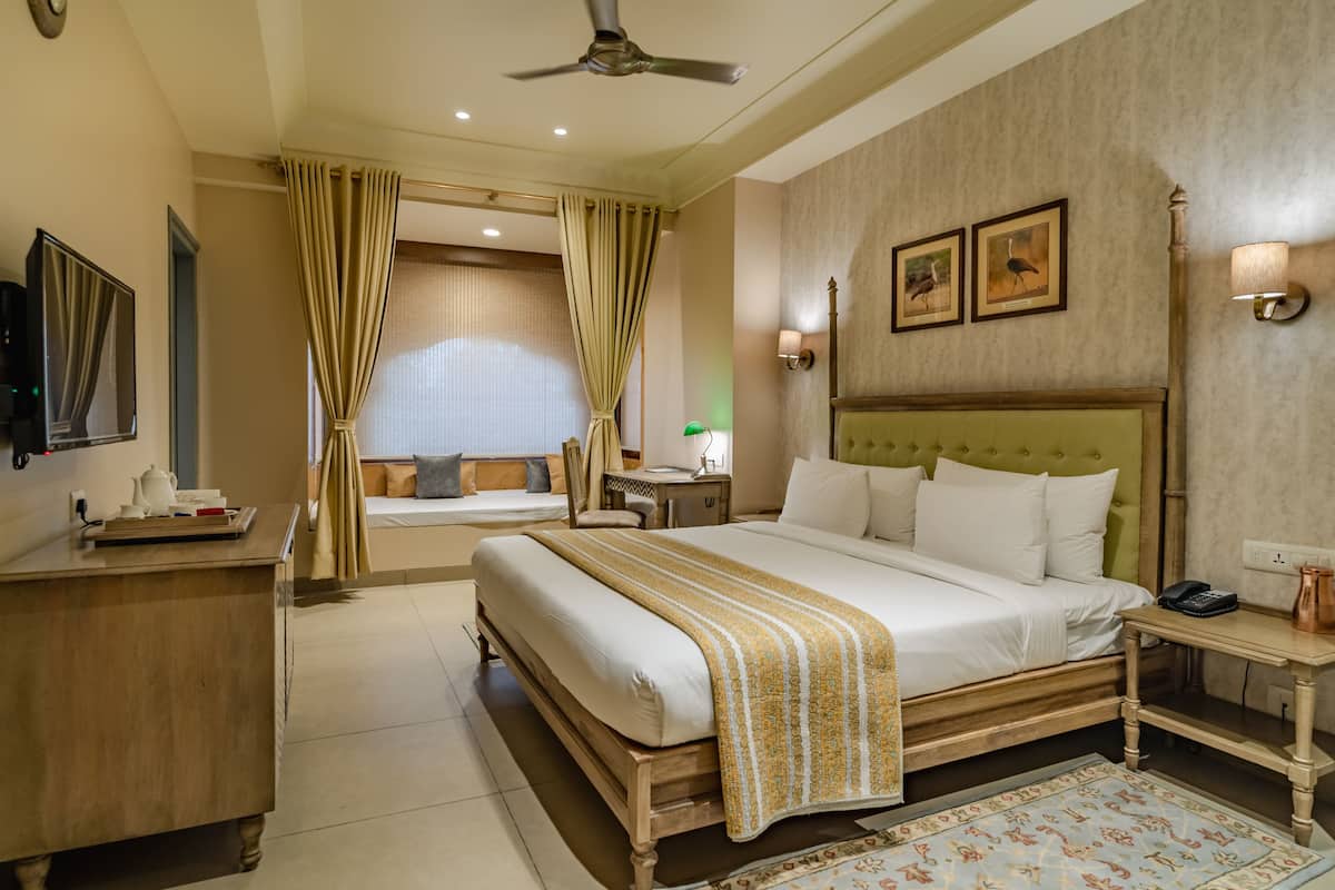 Habitación de hotel con una cama grande, un escritorio, una silla, un televisor y una ventana con cortinas.