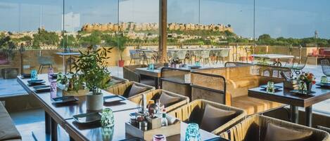 Un área de comedor en la azotea con mesas, sillas y plantas en macetas.