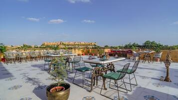 An outdoor terrace with tables and chairs, a view of a historic fort in the background, and a patterned floor.