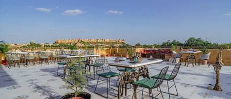 An outdoor terrace with tables and chairs, a view of a historic fort in the background, and a patterned floor.