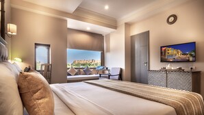 Habitación de hotel con cama, televisión, vista a la ciudad y ventilador de techo.