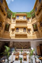 Un patio con arquitectura ornamentada, un área de estar central con sillas y mesas, y plantas en macetas.