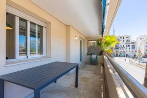 Uma varanda com um banco de madeira, um vaso com planta e vista para a rua.