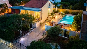 Una proprietà residenziale con piscina, patio coperto e vialetto in pietra che conduce all'ingresso.