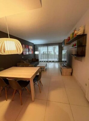 Een moderne woonkamer met een houten eettafel, stoelen, een bank en een televisie op een plank.