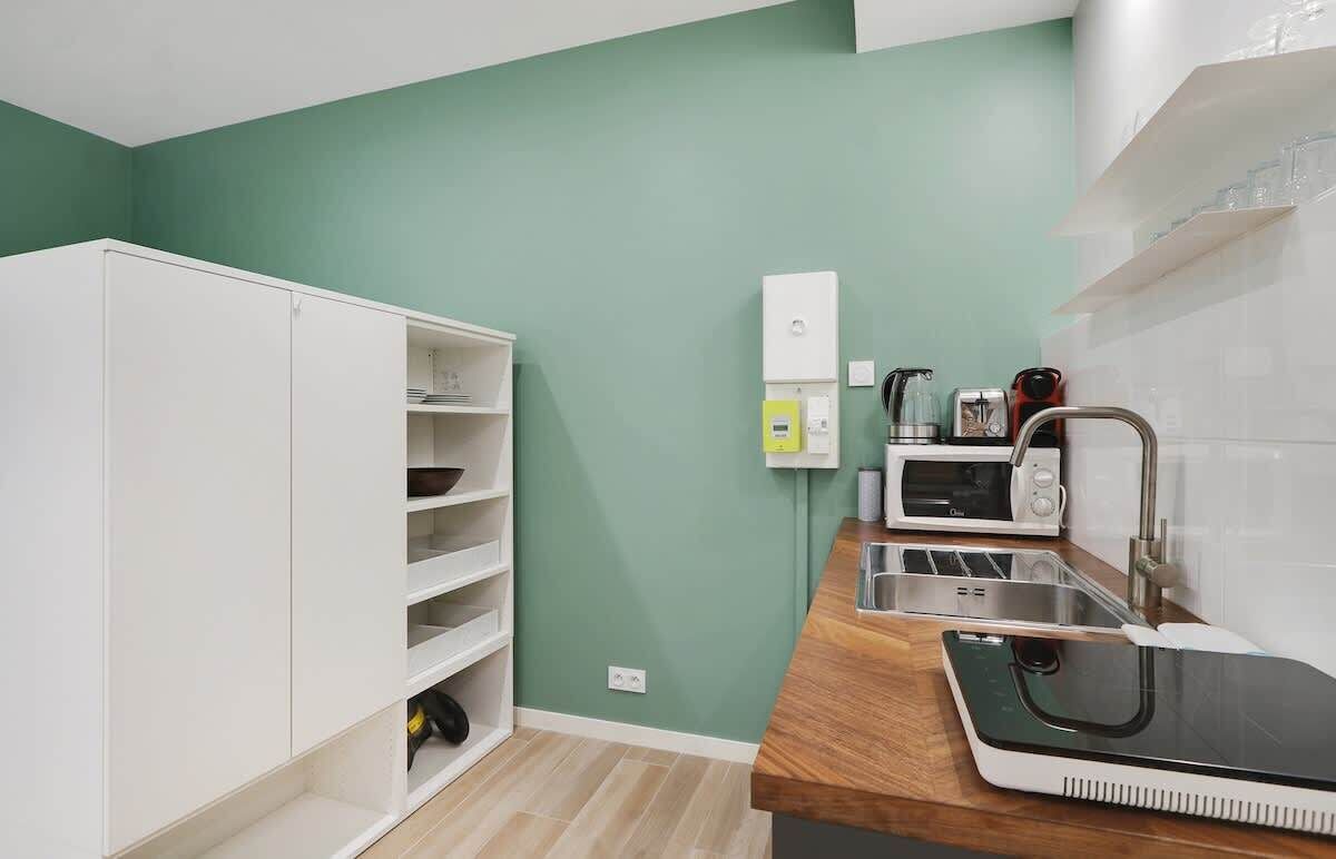 A compact kitchen with white cabinets, a microwave, a kettle, and a sink.