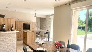 A modern kitchen with wooden cabinets, a dining area with a wooden table set for four, and a large window offering a view of the outdoors. - 10 min from Dinan, large renovated house with garden, 4 bedrooms, 3 bathrooms (Saint-Carné)